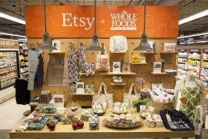 Display of Etsy shop products inside a Whole Foods Market featuring handmade items like tote bags and aprons.