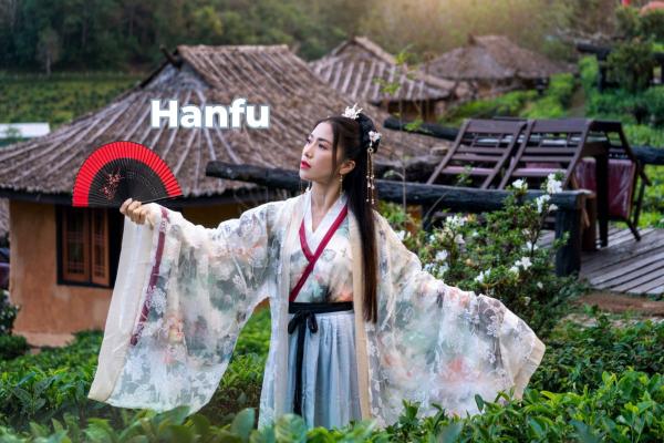 Woman in traditional Hanfu holding a red fan with Chinese-style houses in the background.